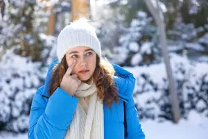 A woman standing outside in the snow with her hand on her nose