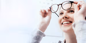 A smiling woman wearing glasses is holding them up to her face in a room.
