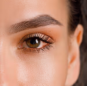 Close-up of a woman's face with her left eye visible, showing well-groomed eyebrows and eyelashes, and a smooth, radiant complexion