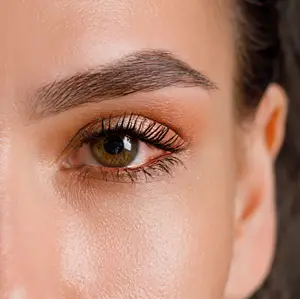 Close-up of a woman's face with her left eye visible, showing well-groomed eyebrows and eyelashes, and a smooth, radiant complexion