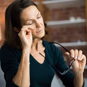 A woman with glasses in her hand, rubbing her eyes