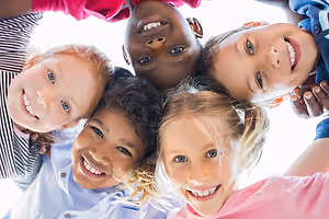 Group of smiling children standing in a circle, each wearing different clothing and looking in different directions.