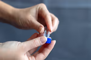 Close up of a person opening a small blue container with a white cap