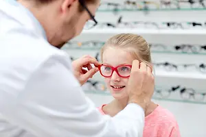 A doctor is adjusting a pair of red glasses on a girl's face.