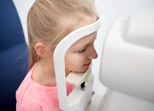 A girl in a pink shirt looking into an eye exam device in a room