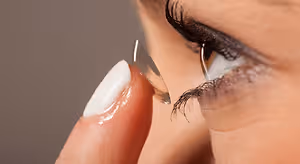 A woman with white nails is adjusting a contact lens on her eye