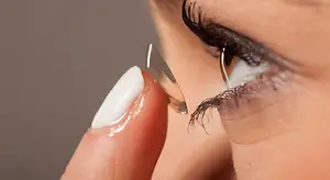 A woman with white nails is adjusting a contact lens on her eye