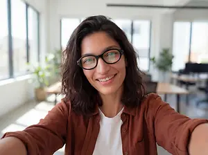 A woman is smiling and posing for a selfie in an office setting.