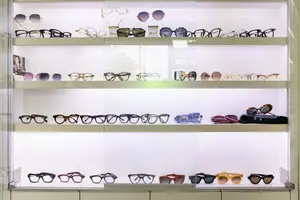 An array of various glasses in different colors and styles displayed on a shelf with a glass cover.