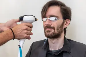 A man wearing glasses with white lenses and a device on his forehead being held by another person