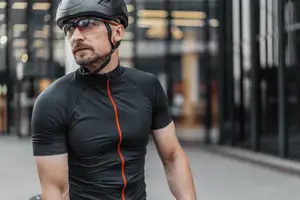A man wearing a black cycling shirt and helmet standing in front of a building