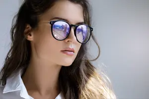 A woman with long hair and wearing glasses standing and looking sideways