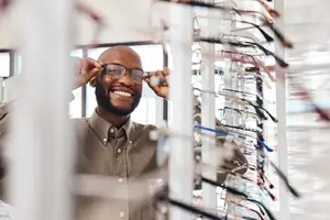 Businessman wearing glasses and smiling at the camera in a store with eyeglasses on display
