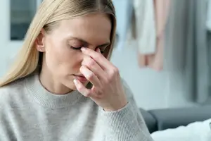 A woman sitting on a couch with her eyes closed and her hand on her nose.