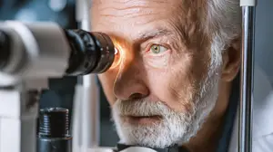 A close up of an elderly man examining his eye with a slit lamp in a clinical setting
