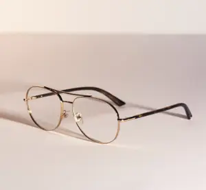A pair of gold-framed glasses with clear lenses on a white surface.