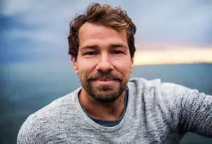 Man smiling and posing for a photo against a blue sky
