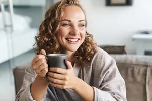 A woman with curly hair smiling and holding a cup