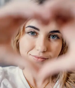 woman smiling with blue eyes and hands making heart shape around her face