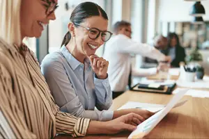 Two women sitting at a desk in an office reviewing a document and smiling