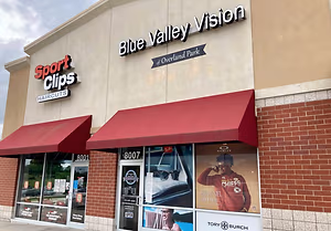 Blue Valley Vision, a sports store, has a red awning, a brick wall, and a sign with a man in a red NFL jersey.