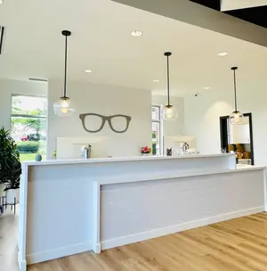 Reception desk at an Overland Park optometrist's office with a pair of glasses hanging on the wall and three lamps hanging from the ceiling.