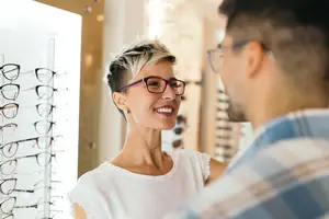 A woman wearing glasses is looking at a man in an optical shop while smiling