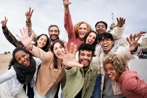 A group of people are posing for a photo with their hands raised, smiling and laughing on a cloudy day.