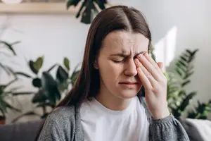 A woman sitting on a couch with her eyes closed and her hand on her forehead