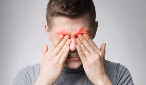Close-up of a man with a red eye, holding his face in pain