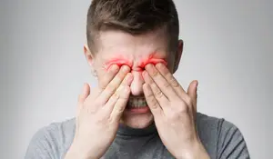 Close-up of a man with a red eye, holding his face in pain