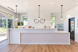 A white reception area in a modern office with wooden floors, large windows, and a hanging pair of glasses