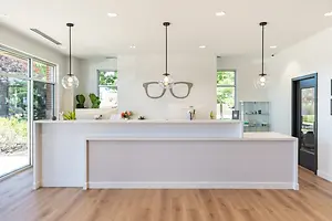 A white reception area in a modern office with wooden floors, large windows, and a hanging pair of glasses