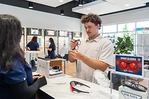 A man is looking at glasses in an optician shop while a woman looks at him