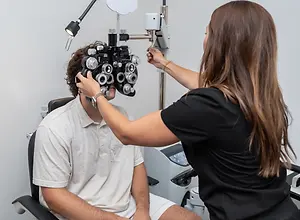 A woman optometrist examining a man's eyes with an ophthalmoscope in an eye clinic.