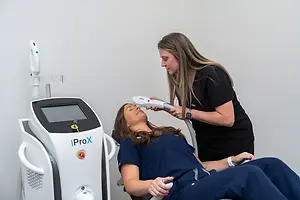 A woman is getting her face treated with a laser device in a salon