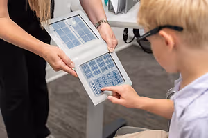 A boy with glasses uses a keyboard with a woman behind him in a room