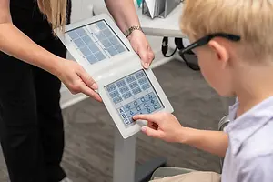 A boy with glasses uses a keyboard with a woman behind him in a room