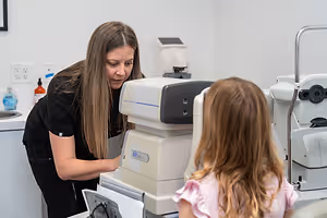 An adult woman is adjusting a machine on a young girl who is sitting in front of it.