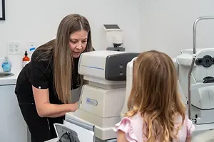 An adult woman is adjusting a machine on a young girl who is sitting in front of it.