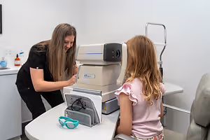 An eye doctor is checking the eye of a girl using a machine in a clinic.