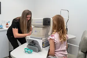 An eye doctor is checking the eye of a girl using a machine in a clinic.