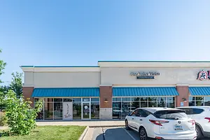 Blue Valley Vision is the name of the establishment. The name is written in blue on the wall, and a white car is parked in front of the establishment.