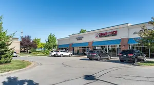 A car is parked on the road in front of a store with trees on the sides.