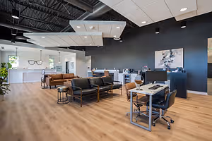 A modern office with a wooden floor and a wooden desk, a black leather couch, and a potted plant in the corner.