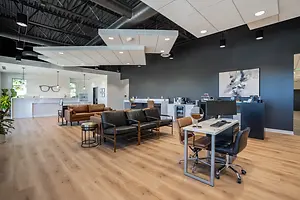A modern office with a wooden floor and a wooden desk, a black leather couch, and a potted plant in the corner.
