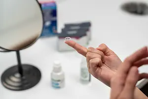 A person is touching a contact lens with their finger in front of a mirror.