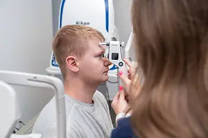 A young man has his eyes examined by a woman using a Nikon device