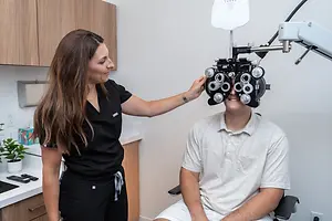 A woman is adjusting the ophthalmoscope on a man sitting in a chair in an indoor area.