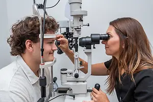 A man is having his eyes examined by a woman optometrist using a slit lamp.